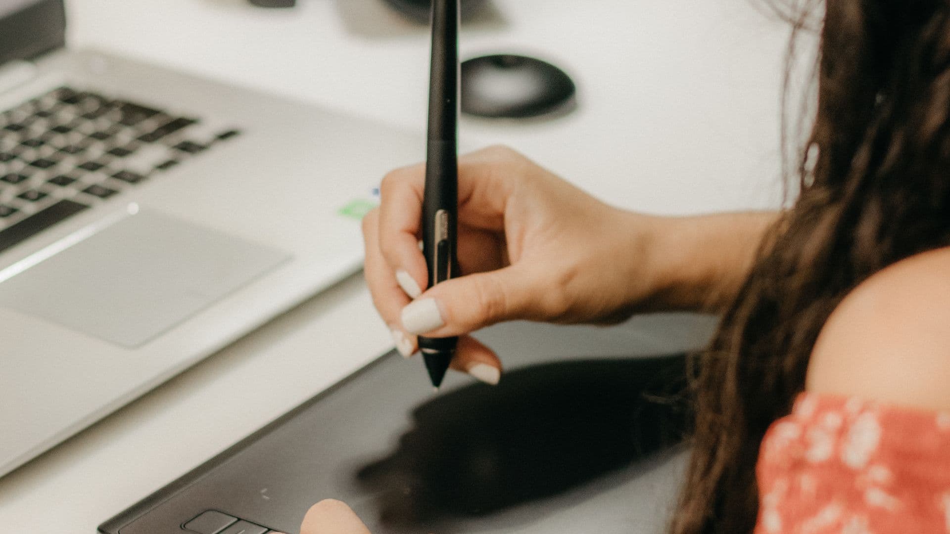 A designer uses a stylus on a graphics tablet beside a laptop.
