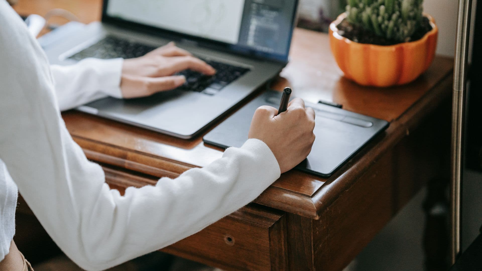 A person uses a stylus and graphics tablet beside a laptop.
